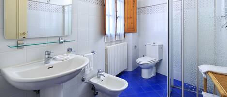 Une salle de bain avec un lavabo blanc, un bidet, des toilettes et une douche à parois de verre.
