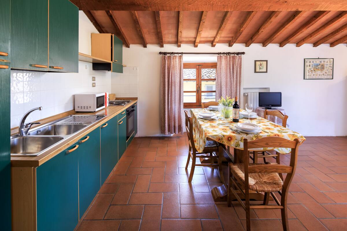 Une cuisine avec des armoires de couleur turquoise, un plafond en bois, une table à manger avec des chaises et un téléviseur dans un coin.