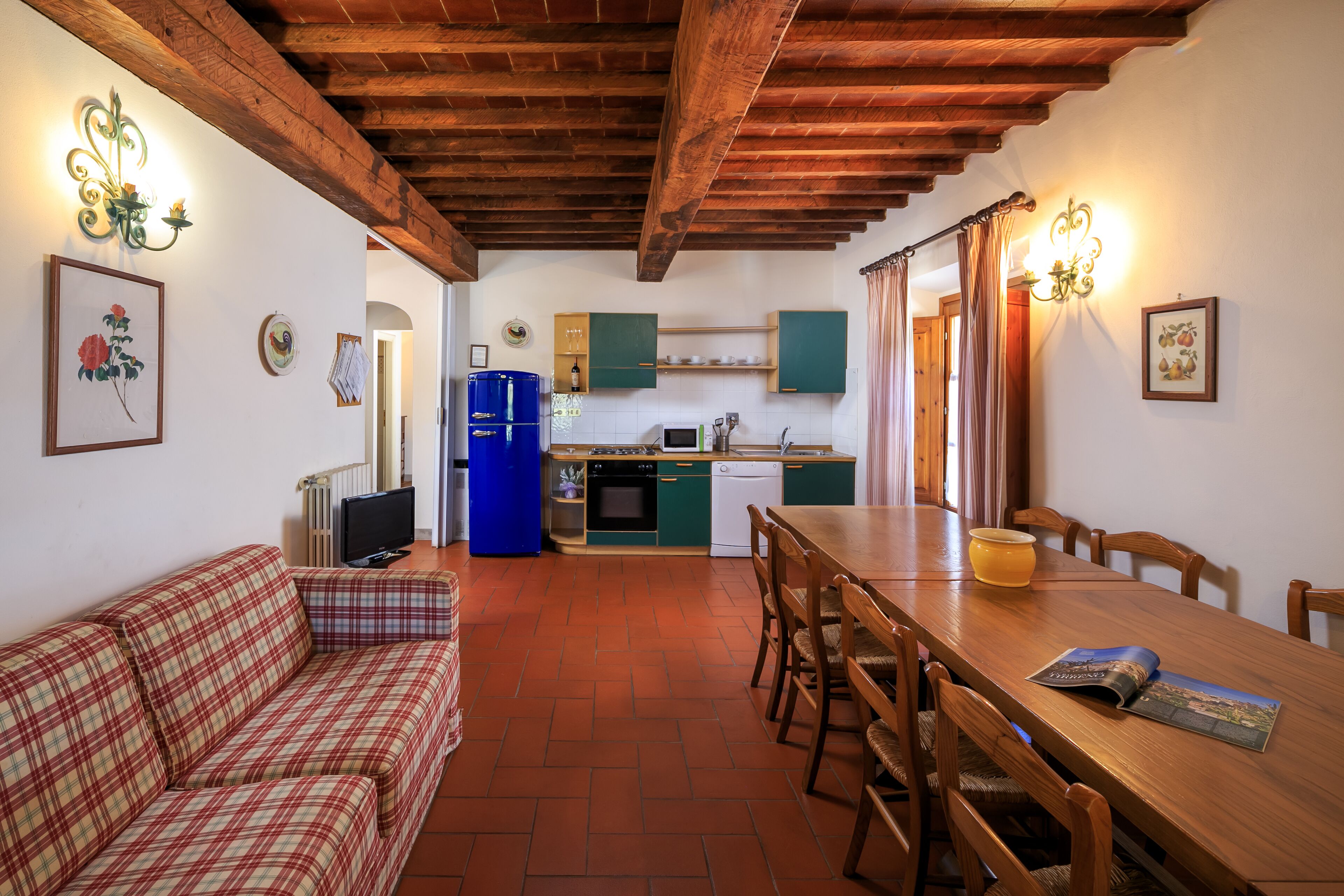 Una cocina acogedora con vigas de madera, una mesa de comedor con sillas, un sofá y un televisor.