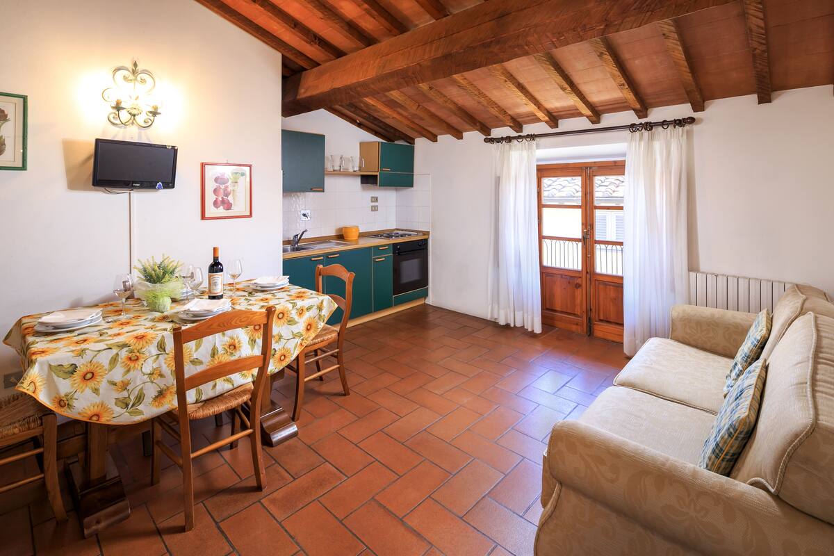 Un coin repas avec une table dressée pour quatre personnes, un canapé et une cuisine en arrière-plan.