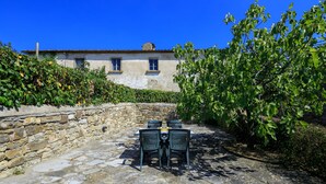 Une terrasse en pierre avec une table et des chaises, un mur en pierre et un bâtiment doté de fenêtres et d’un toit en tuiles.