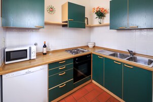 Una cocina con gabinetes verdes, microondas, lavavajillas, estufa y pileta.