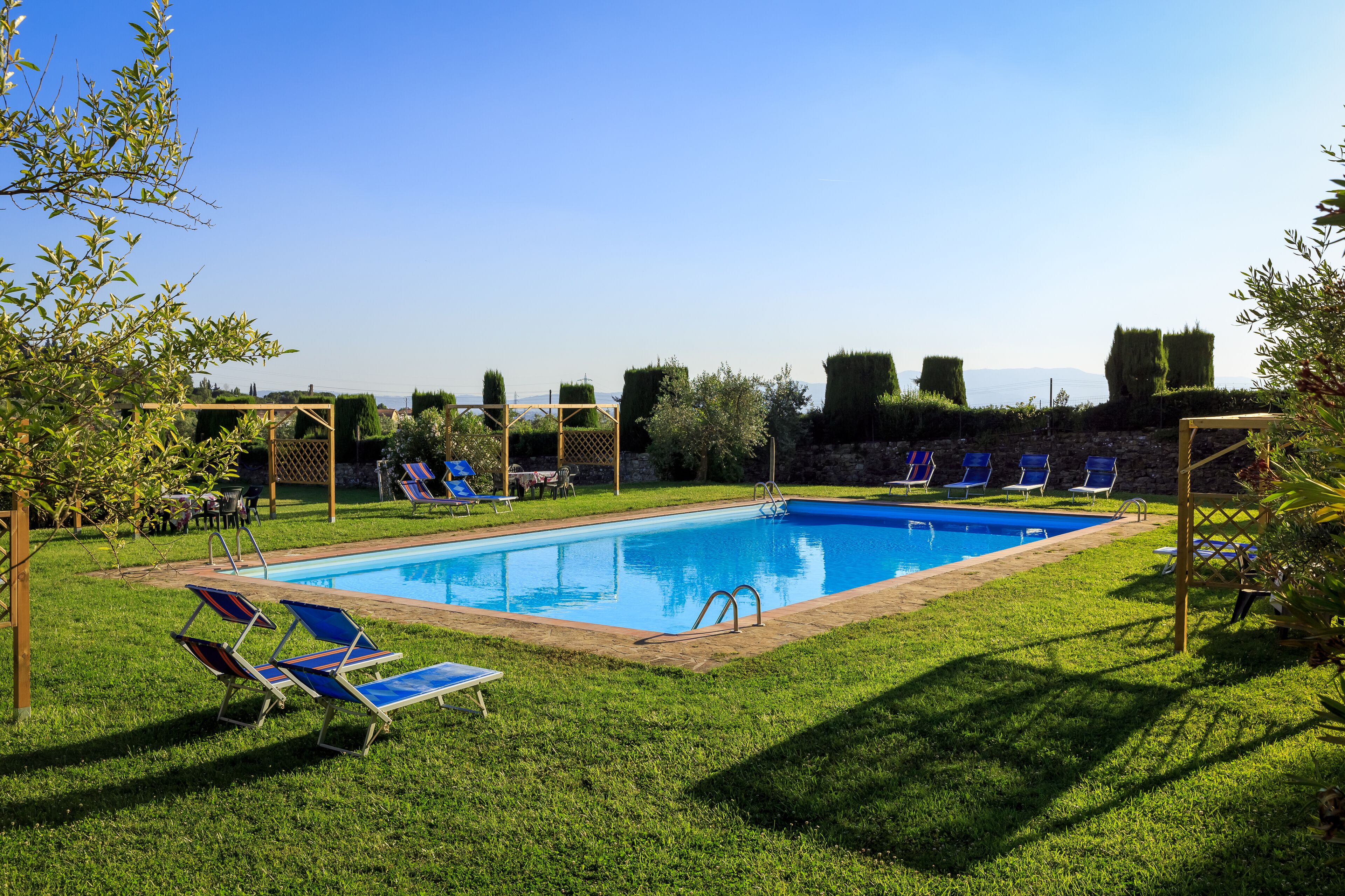 Une piscine rectangulaire dotée d’une terrasse en bois et de chaises longues.