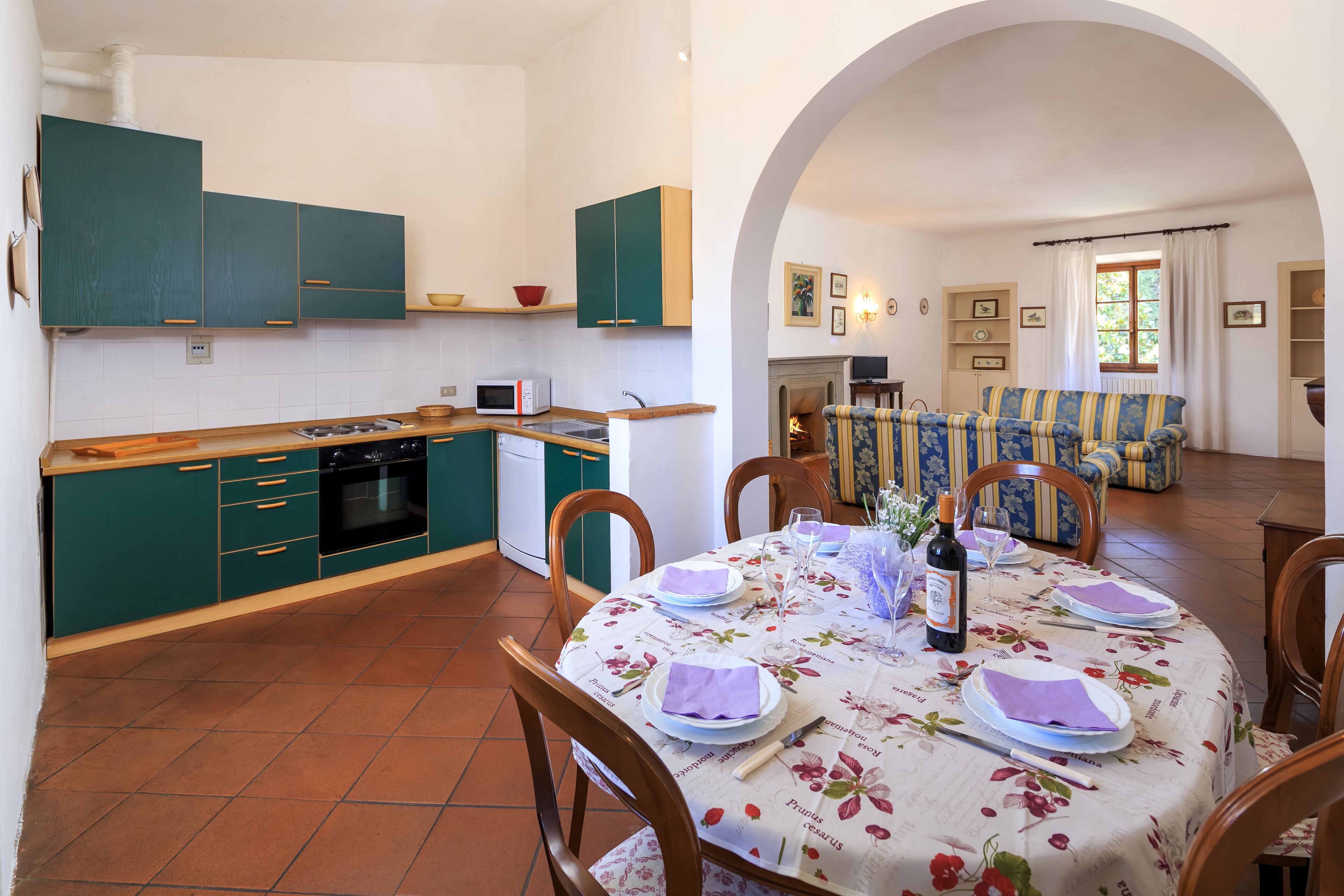 Un coin repas avec une table dressée pour quatre personnes, une cuisine avec des meubles de couleur turquoise et un salon avec un canapé et des fauteuils.