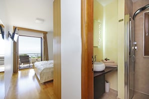 Une chambre d’hôtel avec un balcon, un lit, une salle de bain avec un lavabo et un miroir, et un espace douche.