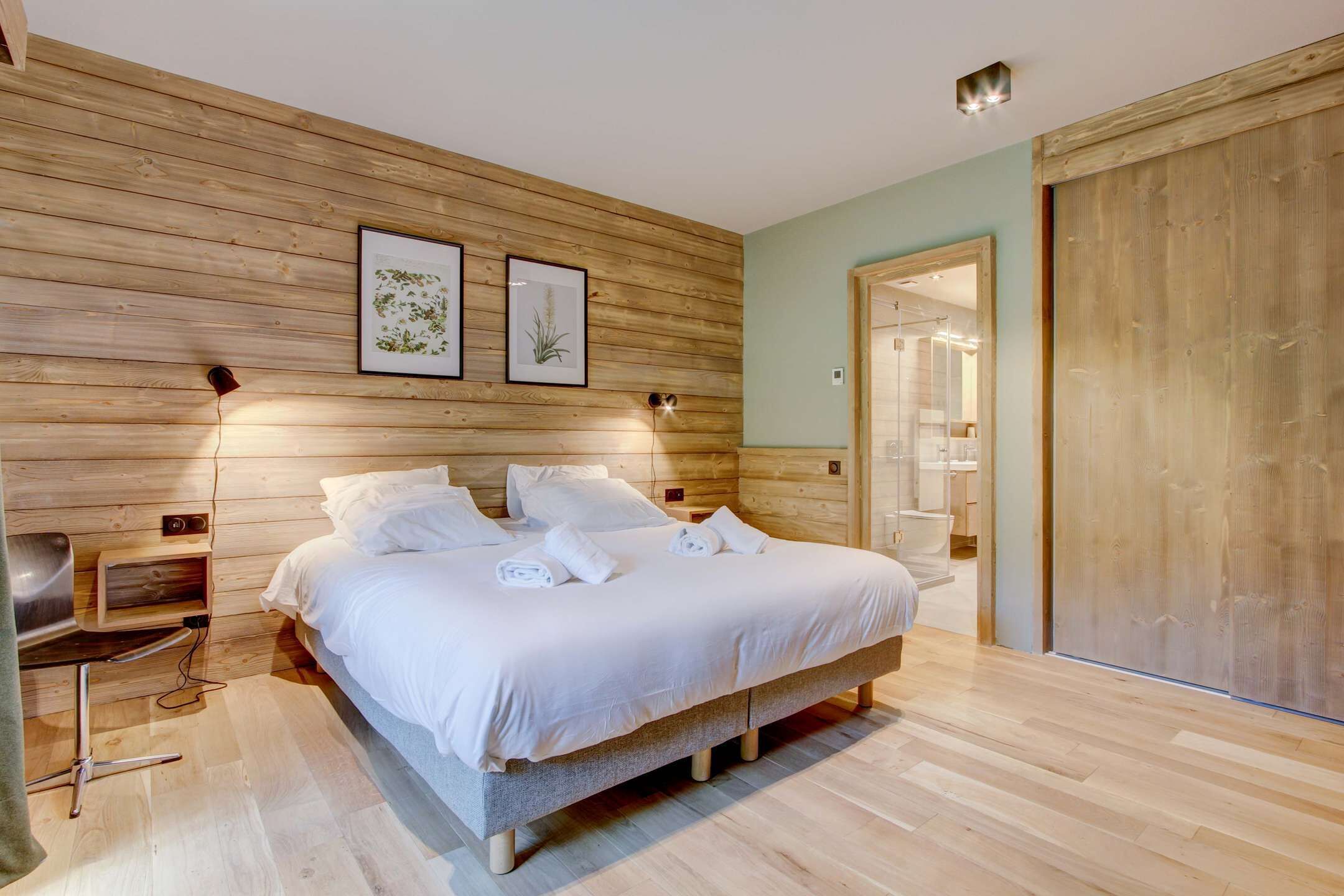 Ein Schlafzimmer mit einem hölzernen Kopfteil, einem Bett mit weißer Bettwäsche, einem Nachttisch mit Lampe und einem gerahmten Pflanzenprint an der Wand.