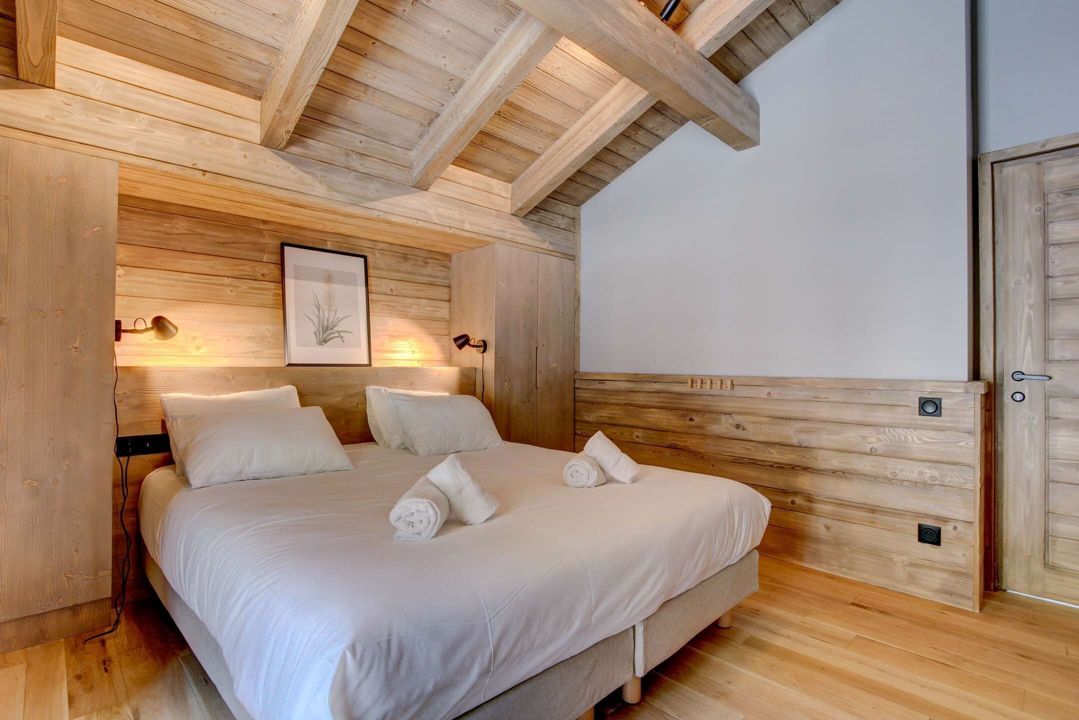 Ein Schlafzimmer mit Holzboden, einem Bett mit weißer Bettwäsche und einem gerahmten Bild an der Wand.