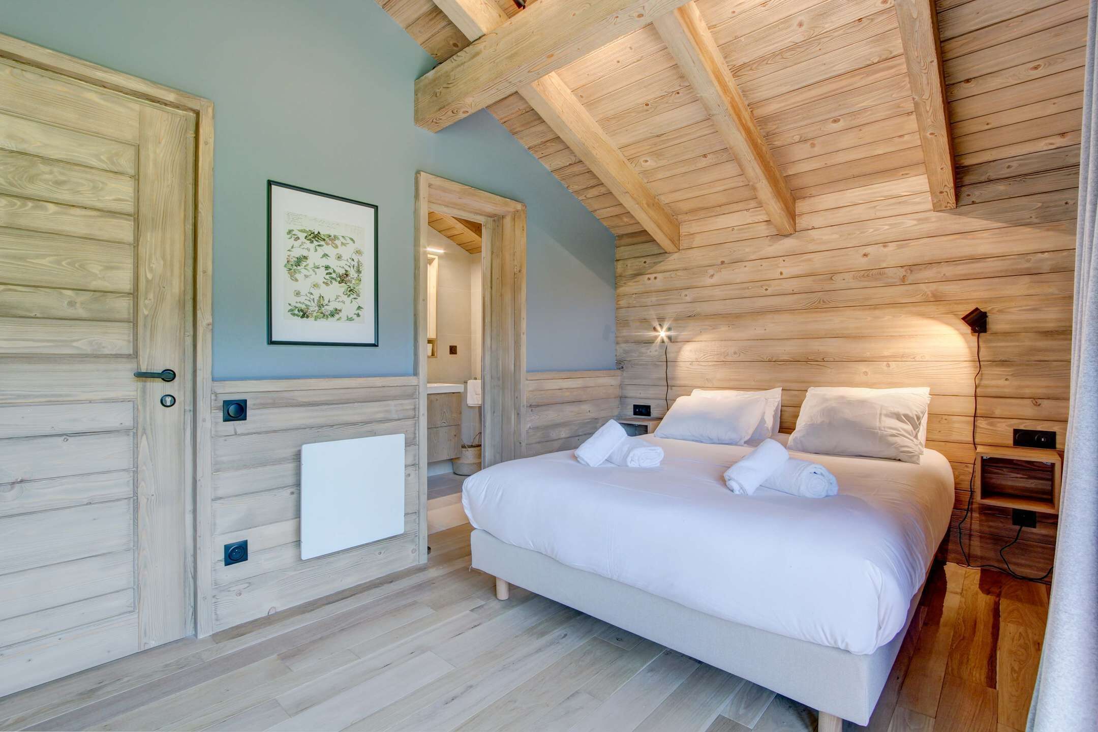 A bedroom with a wooden ceiling, a bed with white linens, and a framed botanical print on the wall.