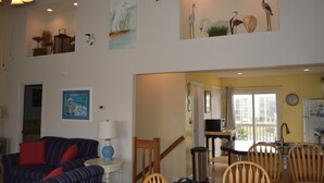 A living room with a sofa, a dining table with chairs, a staircase, and a kitchen area. - 5 BR Nags Head second row beach house  (Nags Head)