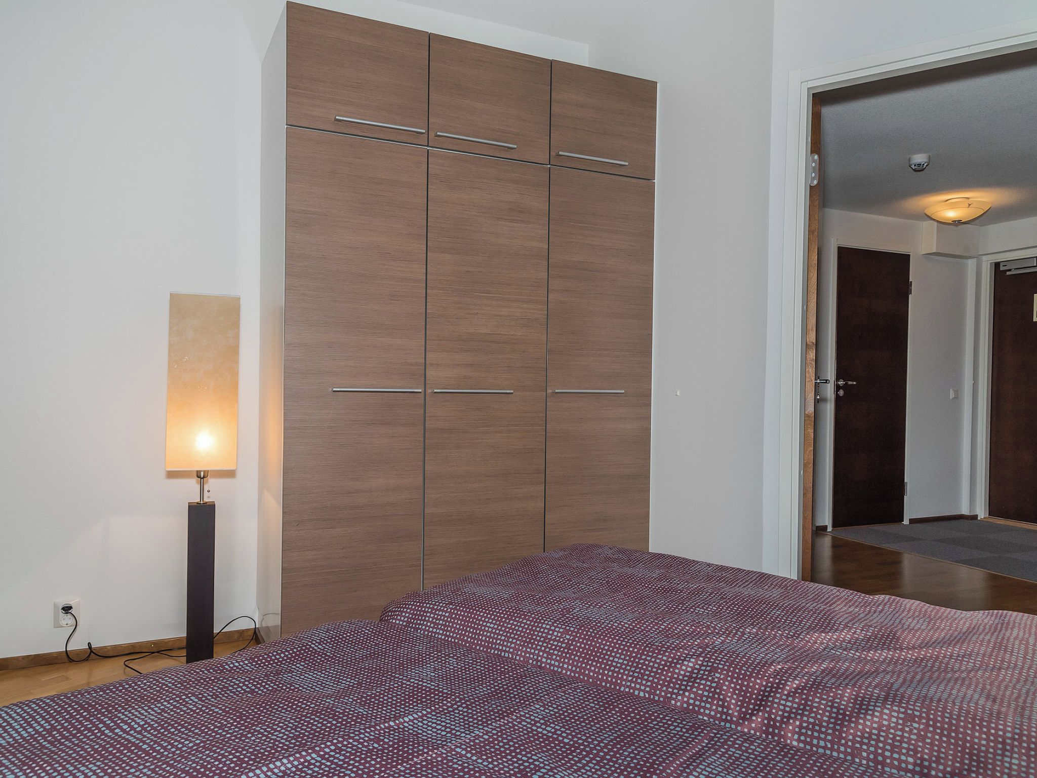 Een slaapkamer met een grote kledingkast, een bedlampje en een geborduurde spreidekker.