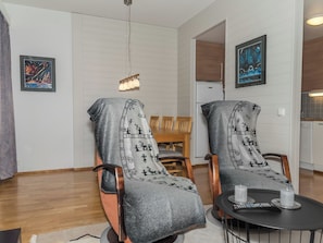 A modern living room with two armchairs covered in a blanket, a dining table with chairs, a small round table with a remote control, and artwork on the walls. - Ylläs chalets 2301 by Interhome (Ylläsjärvi)