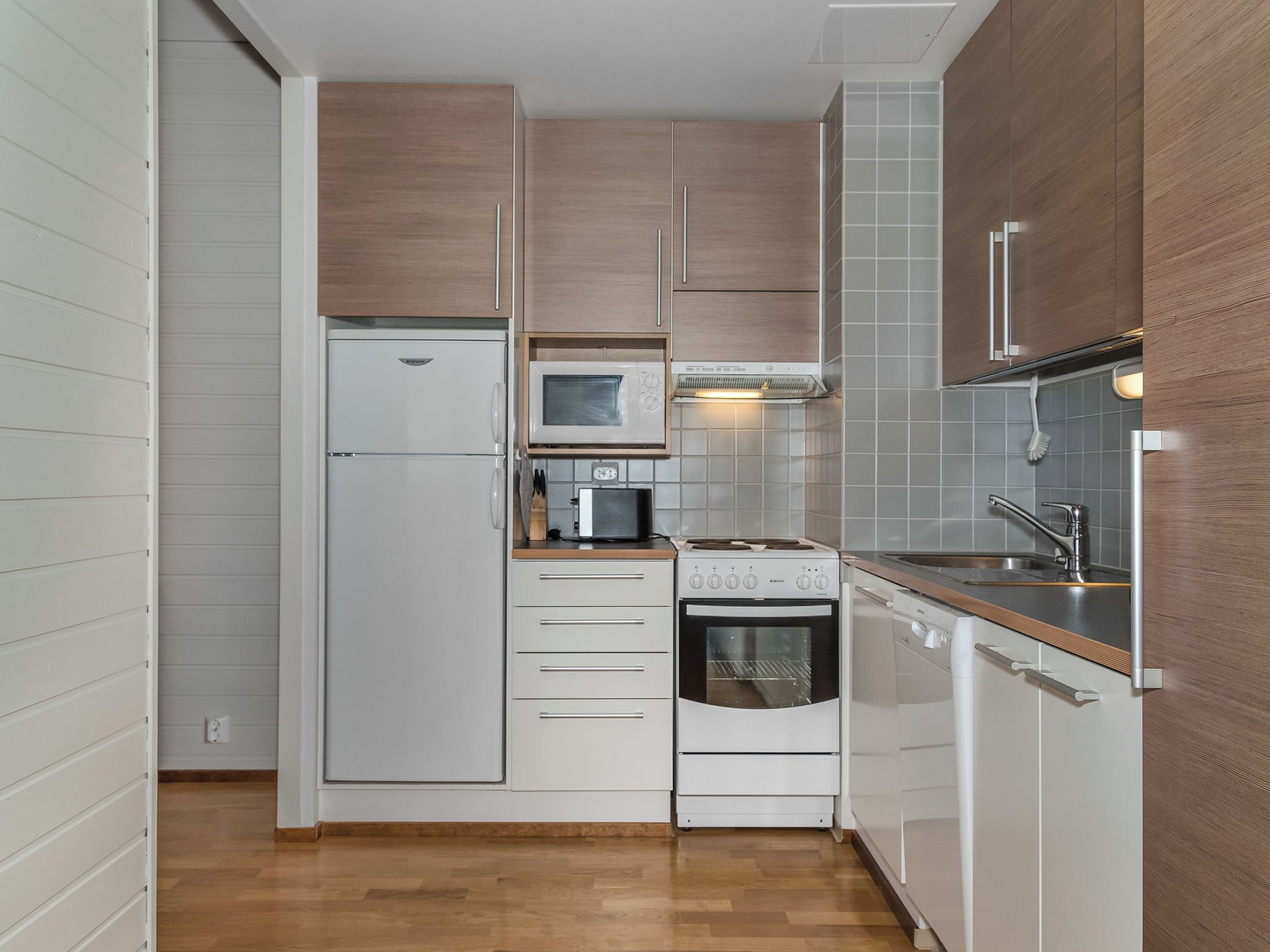 Une cuisine compacte avec des meubles blancs, un four à micro-ondes encastré, une cuisinière et un lave-vaisselle.