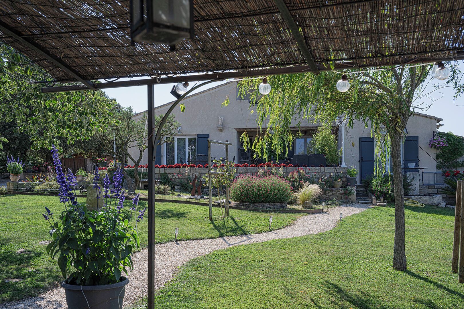 Un espace extérieur abrité, avec un chemin menant à un bâtiment doté d’une façade en pierre et de volets bleus.