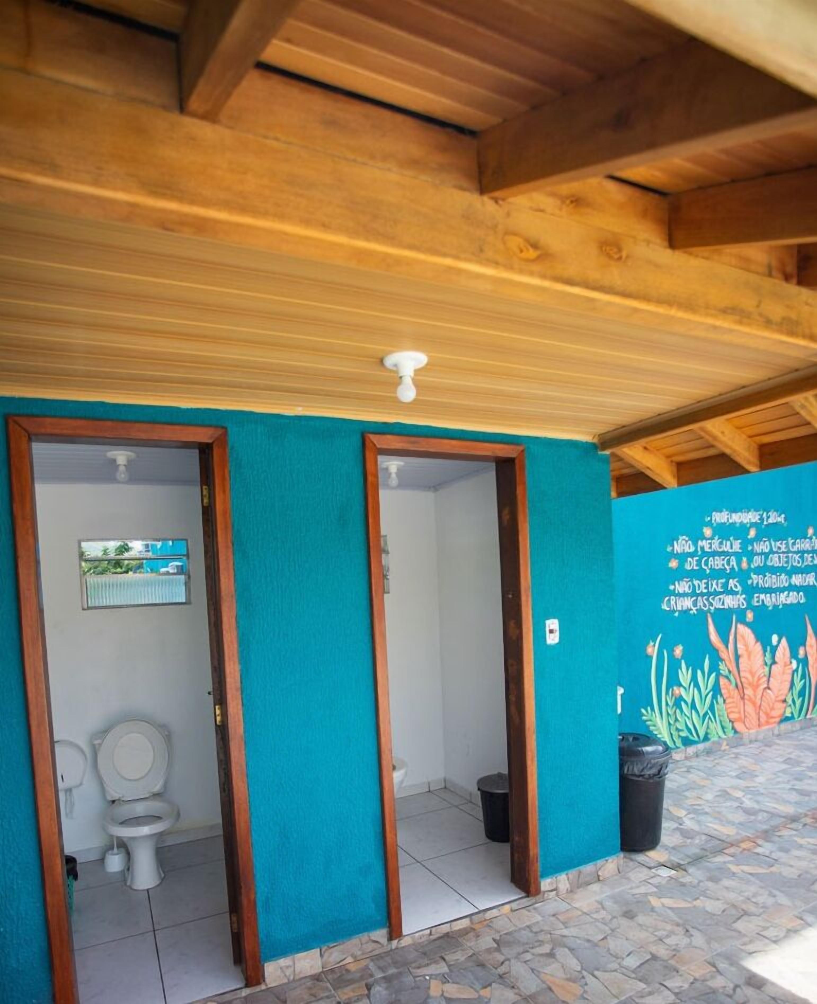 Une salle de bain avec deux toilettes, un luminaire au plafond et un mur orné d’une fresque colorée.