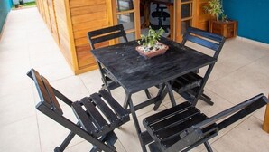 A wooden outdoor dining area with a table and chairs, a potted plant, and a view of the interior through glass doors. - Paraíso do Estaleirinho - Baln Camboriú (Balneário Camboriú)