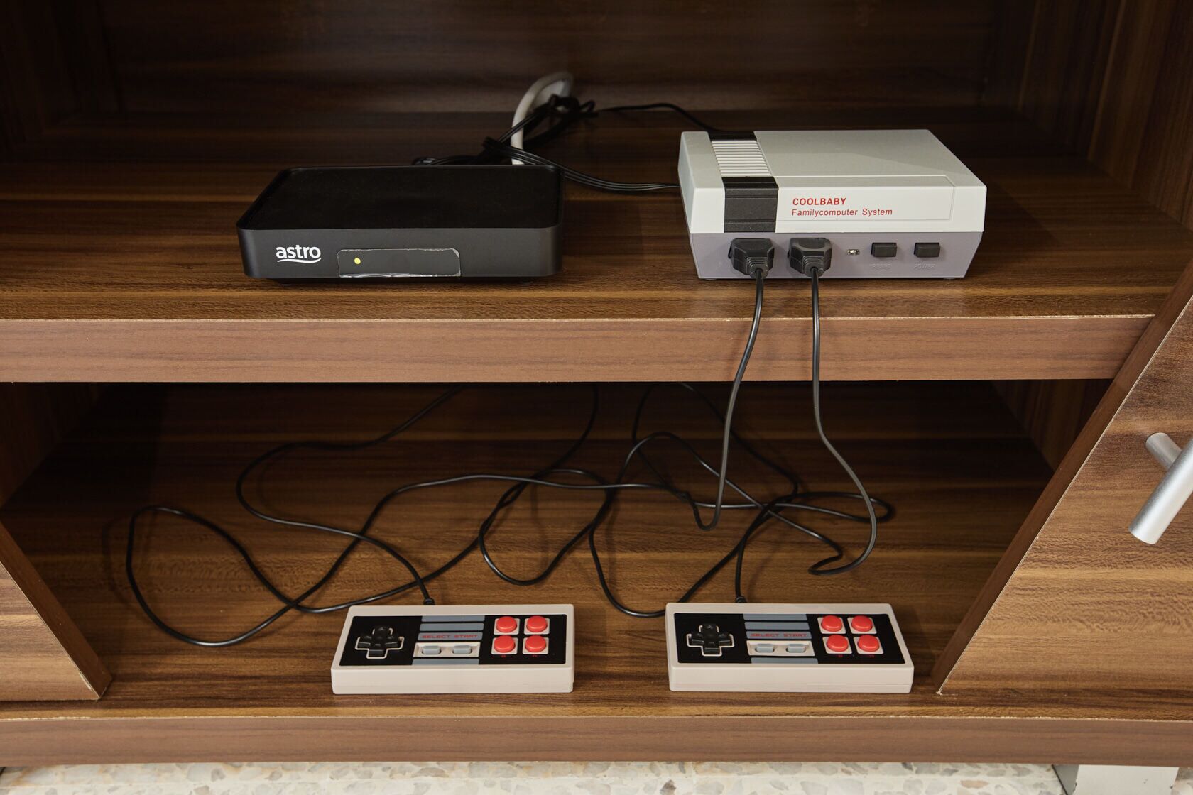 A wooden cabinet with two retro gaming consoles and a family computer system on top.