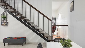 A modern staircase with a metal railing, a grey bench with colorful cushions, and a potted plant on a white table.