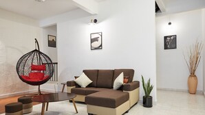 A modern living room with a brown sectional sofa, a red hanging chair, a small round table, and a potted plant.