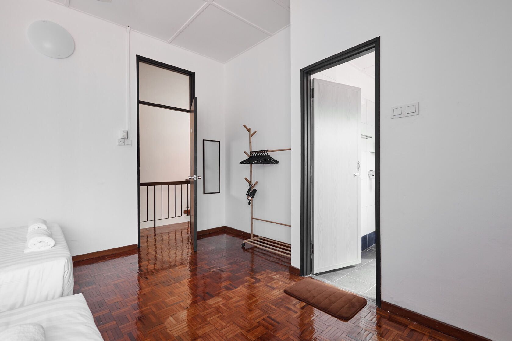 Um corredor com piso de madeira, parede branca, um porta-roupas e uma porta que dá para outro cômodo.
