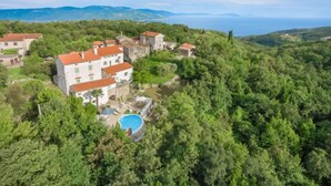 Eine Villa an einem Hang mit mehreren Gebäuden, einem Swimmingpool und üppiger Vegetation.