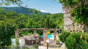 Eine Terrasse mit Pool, Steinboden und Blick auf ein bewaldetes Gebirge.