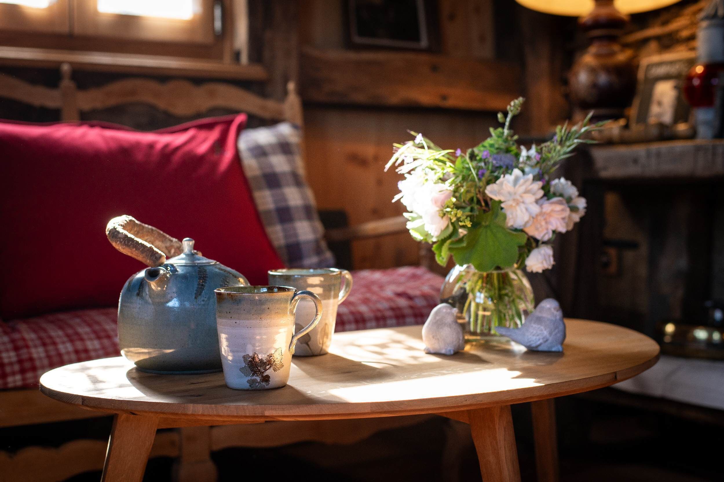A wooden table with a teapot, a mug, and a vase with flowers.