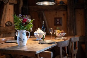 A wooden dining table with a white pitcher of flowers, a teapot, and a bowl of fruit. - La Grange D'hannah - Gîte & Chambre D'hôtes de Charme (Orbey)