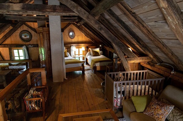 Une chambre mansardée au charme rustique, avec des poutres apparentes, un lit en mezzanine et un coin salon confortable agrémenté de coussins.