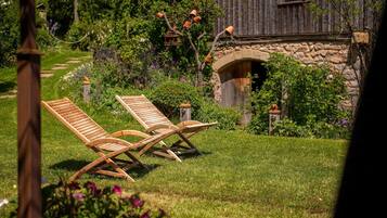 Dos sillones de madera en un jardín con un muro de piedra y un edificio de madera al fondo.