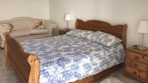Een slaapkamer met een houten bed, een nachtkastje van hout, een bedtafel, een lamp, een bank en een bed met een dessin.