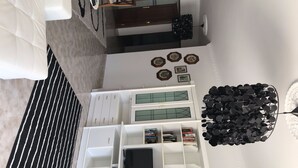 Een ruime woonkamer met een grote, witte entertainmentkast, een zwarte televisie en een decoratieve zwarte kroonluchter.