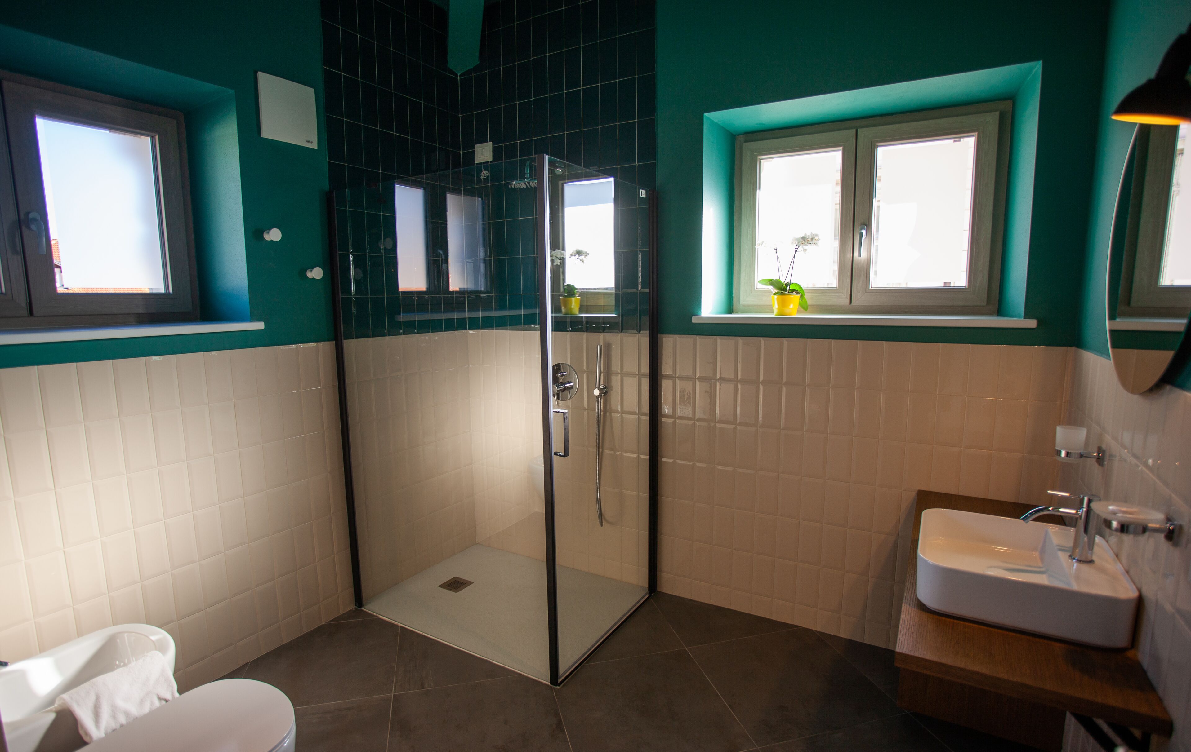 A bathroom with a glass-enclosed shower, a sink, and a window with a plant.