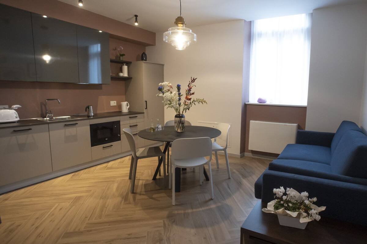 Een moderne keuken met een eettafel, stoelen en een blauwe bank in een woongedeelte.