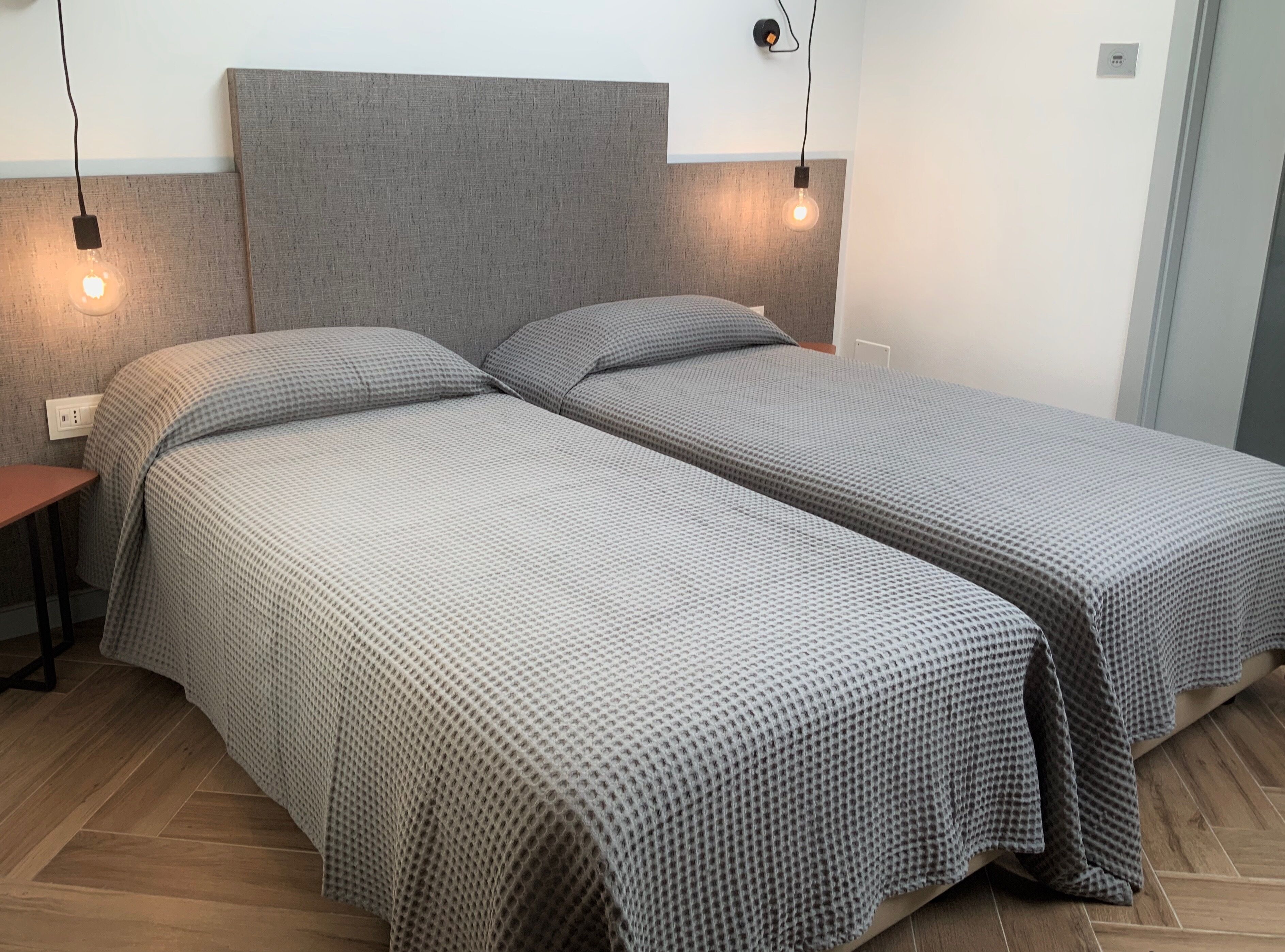 A double bed with a grey headboard and two bedside tables, each with a light bulb.