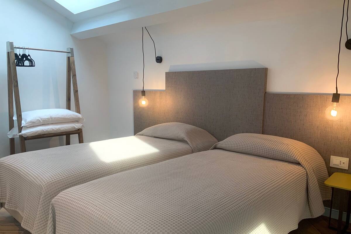 Een kamer met twee bedden, een houten stoel, een kapstok en een klein tafeltje.