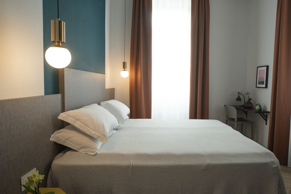 Een hotelkamer met een bed, een bureau, een stoel en een wandlamp.