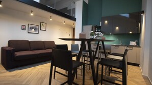 A modern living room with a sofa, chairs, a dining table, and a kitchen area with cabinets and a countertop. - Residenza Alto Garda (Riva del Garda)