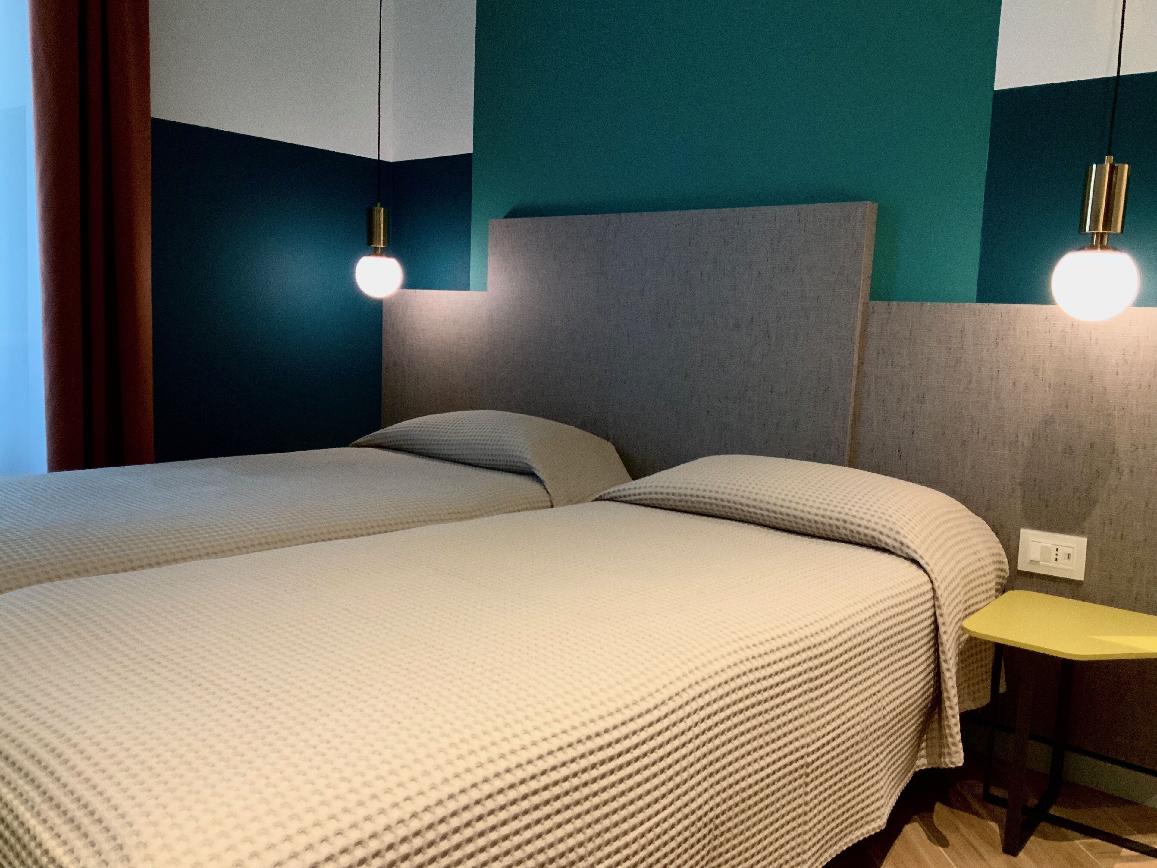 Une chambre d’hôtel moderne avec un grand lit, une petite table et deux lampes fixées au mur.