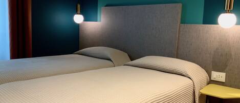 A modern hotel room with a large bed, a small table, and two wall-mounted lights.