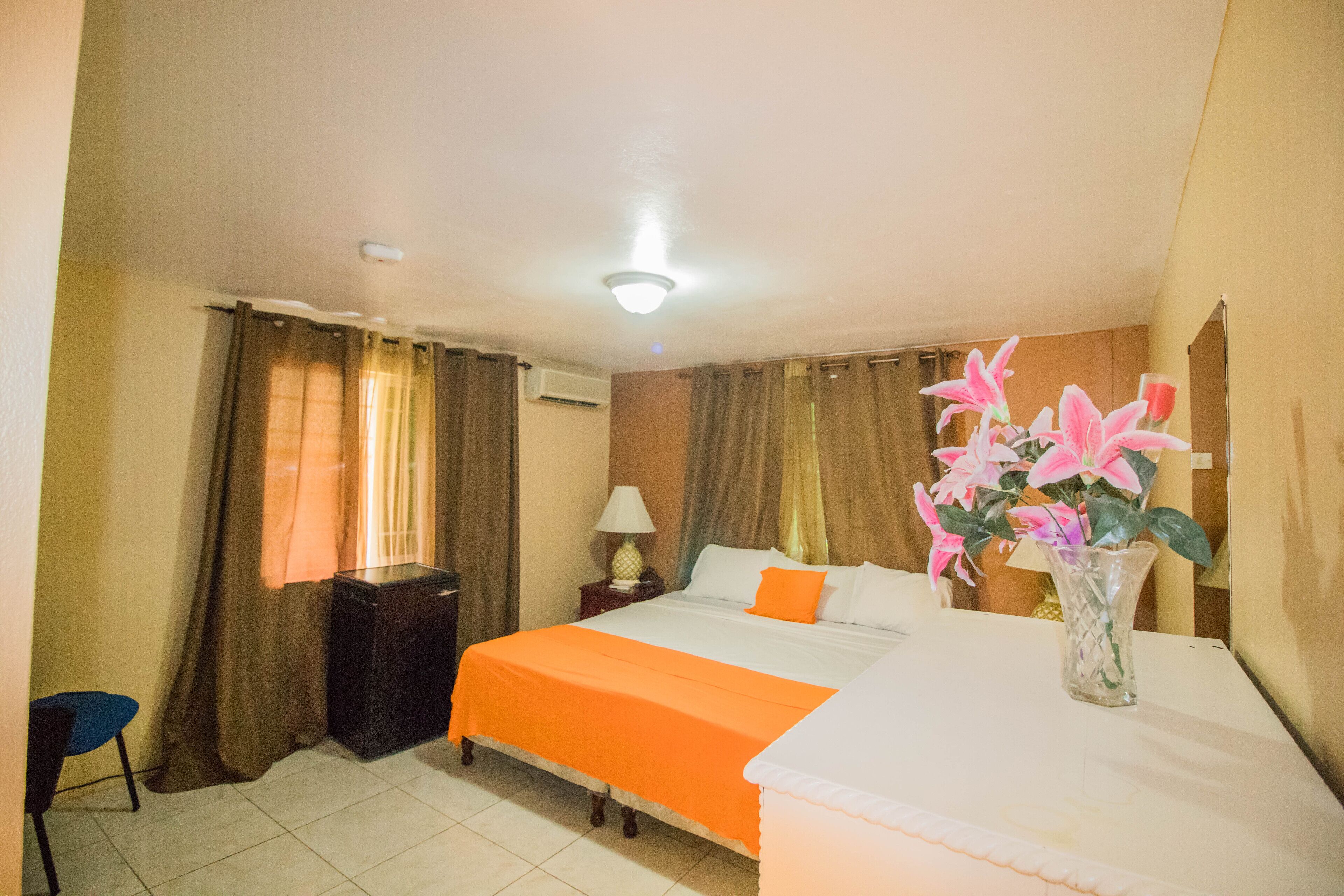 A hotel room with a bed, a nightstand, a lamp, a chair, and a vase with flowers.