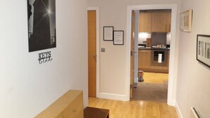 A hallway with a wooden bench, a door leading to a kitchen, and a framed picture on the wall. - Birmingham Garnet, 3 Bedroom Apartment (Birmingham)