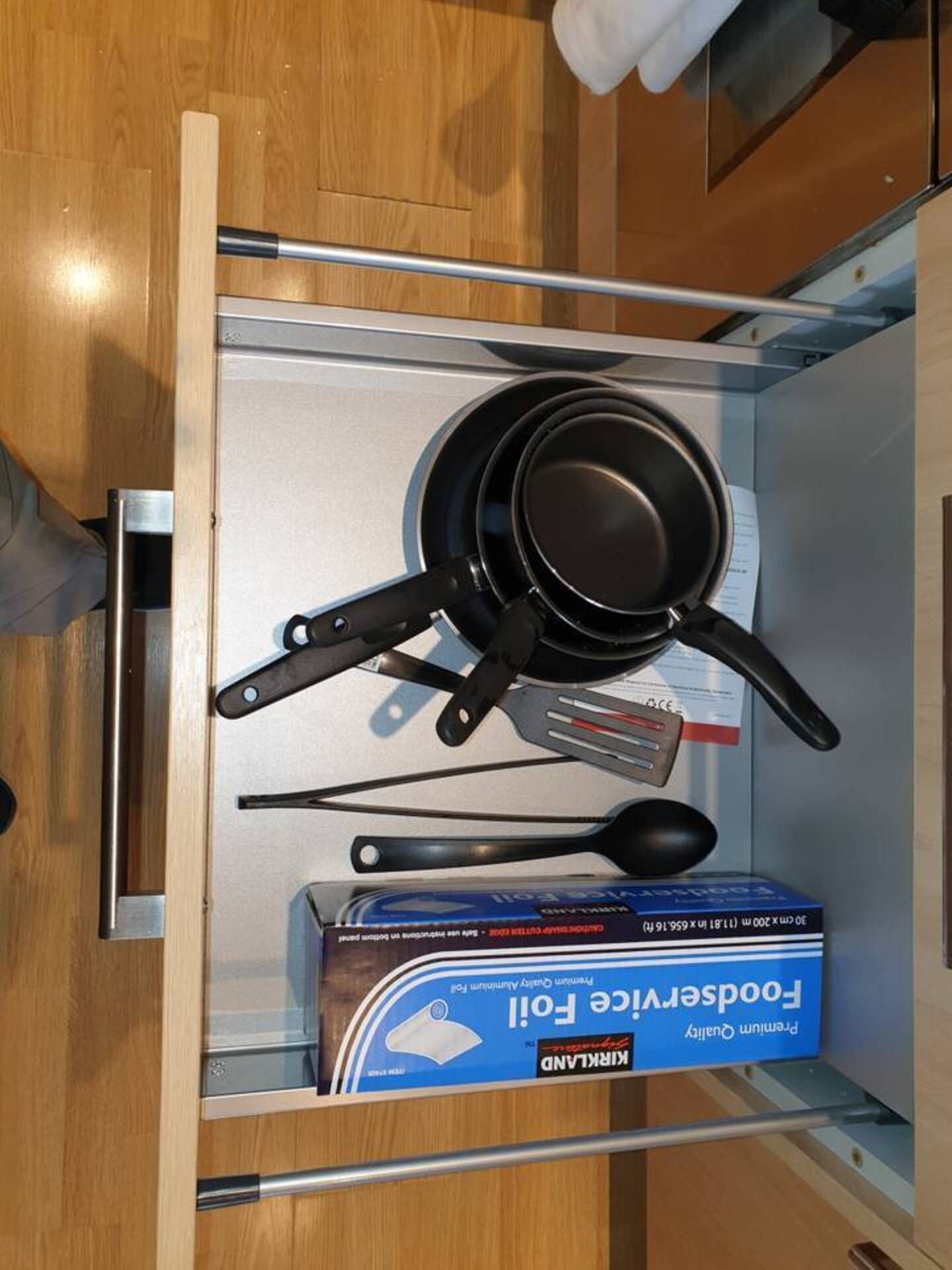 A kitchen drawer with a frying pan, spatula, and a box of foodservice aluminum foil.