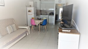 A compact living space with a sofa, a dining table with chairs, a kitchen area, and a television on a stand. - T3 in the heart of the city, on the waterfront, QUIET, Owners nearby (Le Lavandou)