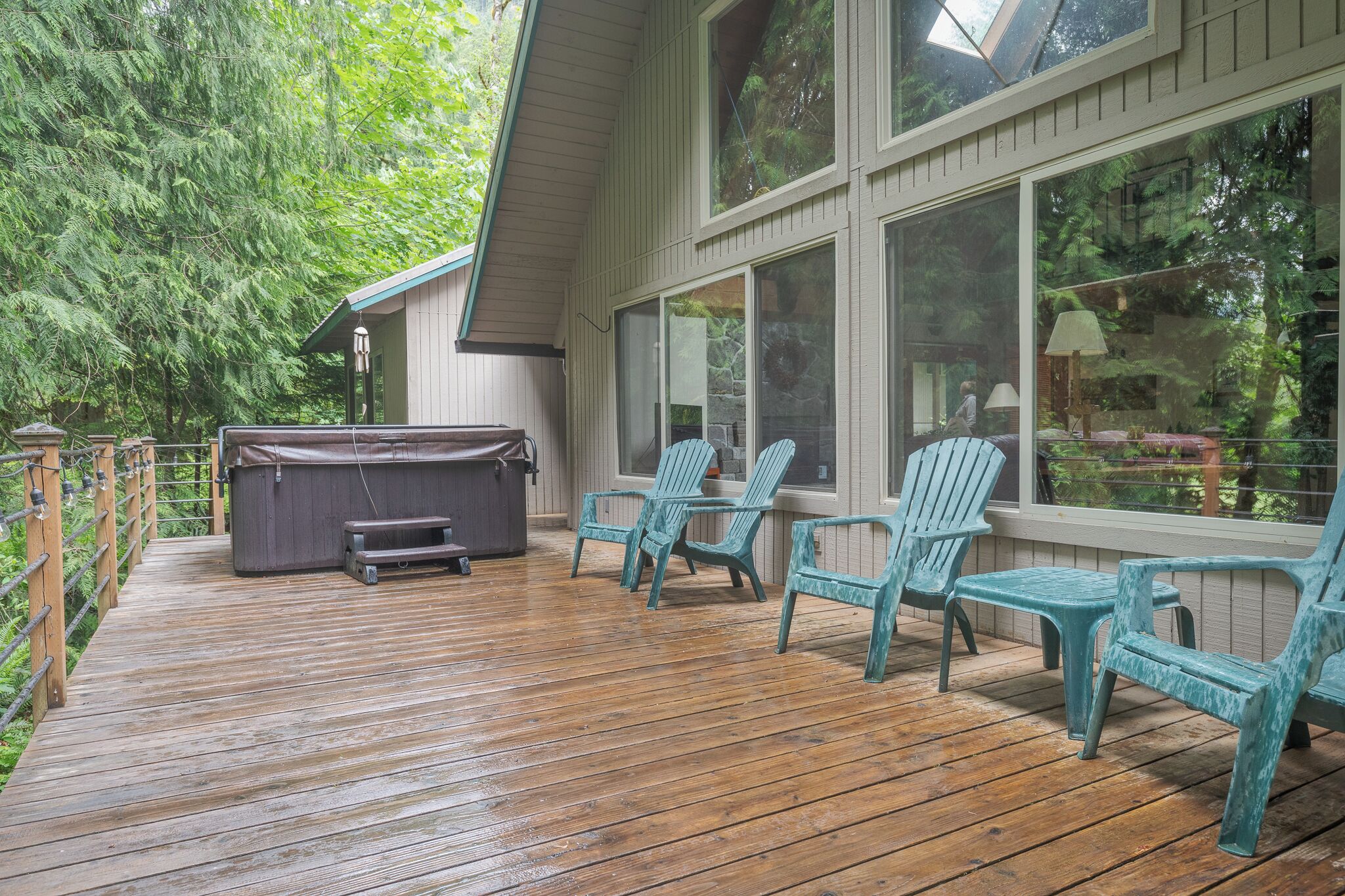 A wooden deck with a hot tub and Adirondack chairs.