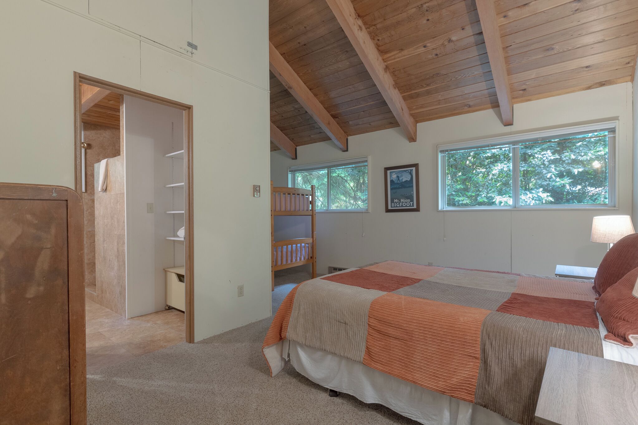 A bedroom with a bed, a wooden ceiling, a window, and a door leading to a bathroom.