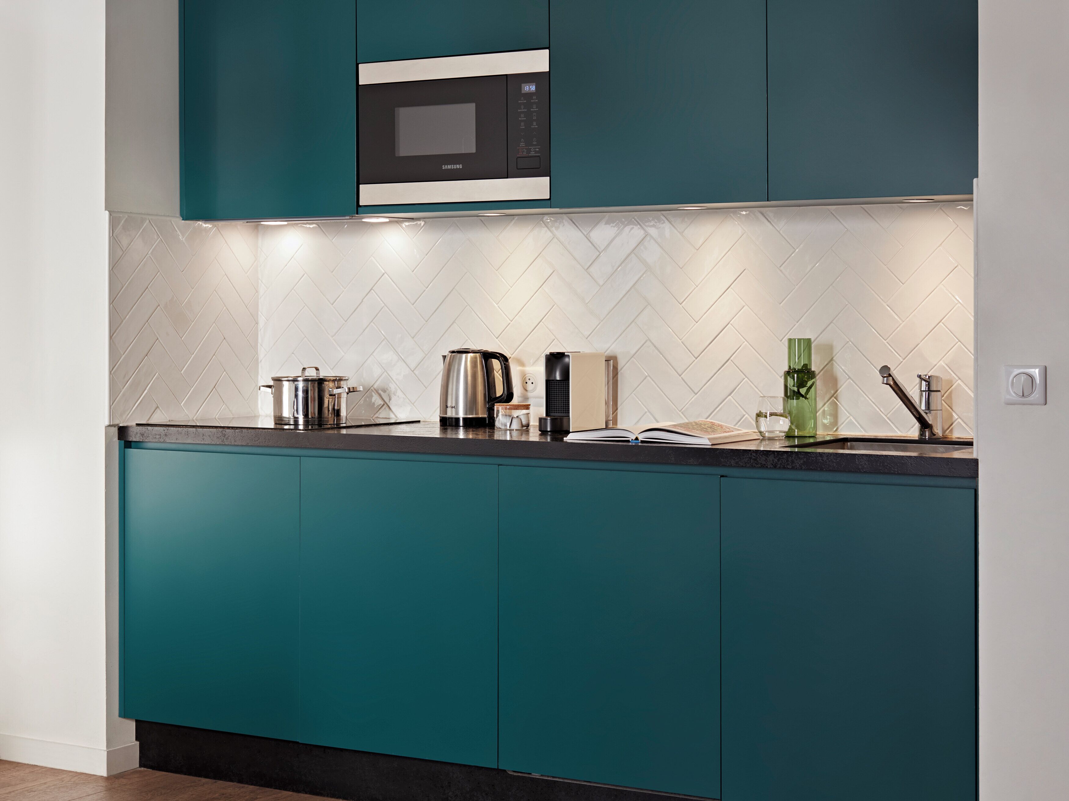 Une cuisine moderne avec des meubles de couleur turquoise, un four à micro-ondes, une bouilloire et une machine à café posés sur le plan de travail.