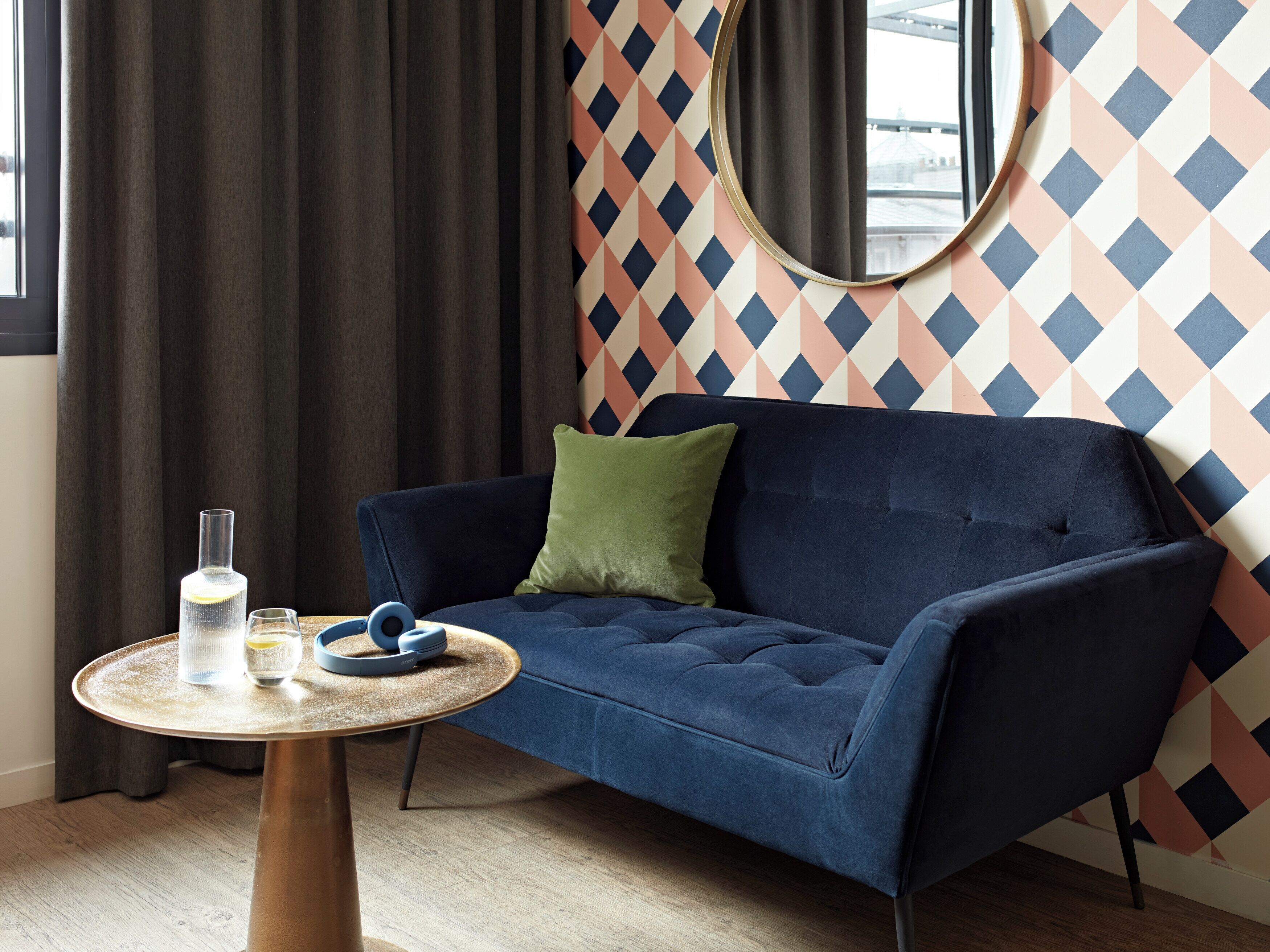 A modern living room with a dark blue sofa, a round wooden coffee table, and a patterned wall.