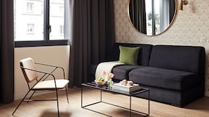 A modern living room with a dark sofa, a round mirror, a glass coffee table, and a chair.