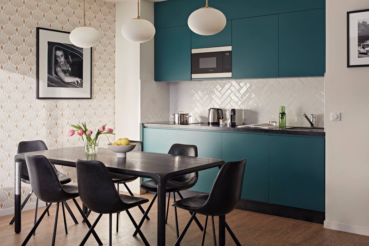 Une cuisine moderne avec des meubles de couleur turquoise, un plan de travail noir et un coin repas comprenant quatre chaises noires.