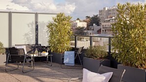 A rooftop terrace with outdoor seating, potted plants, and a cityscape view.